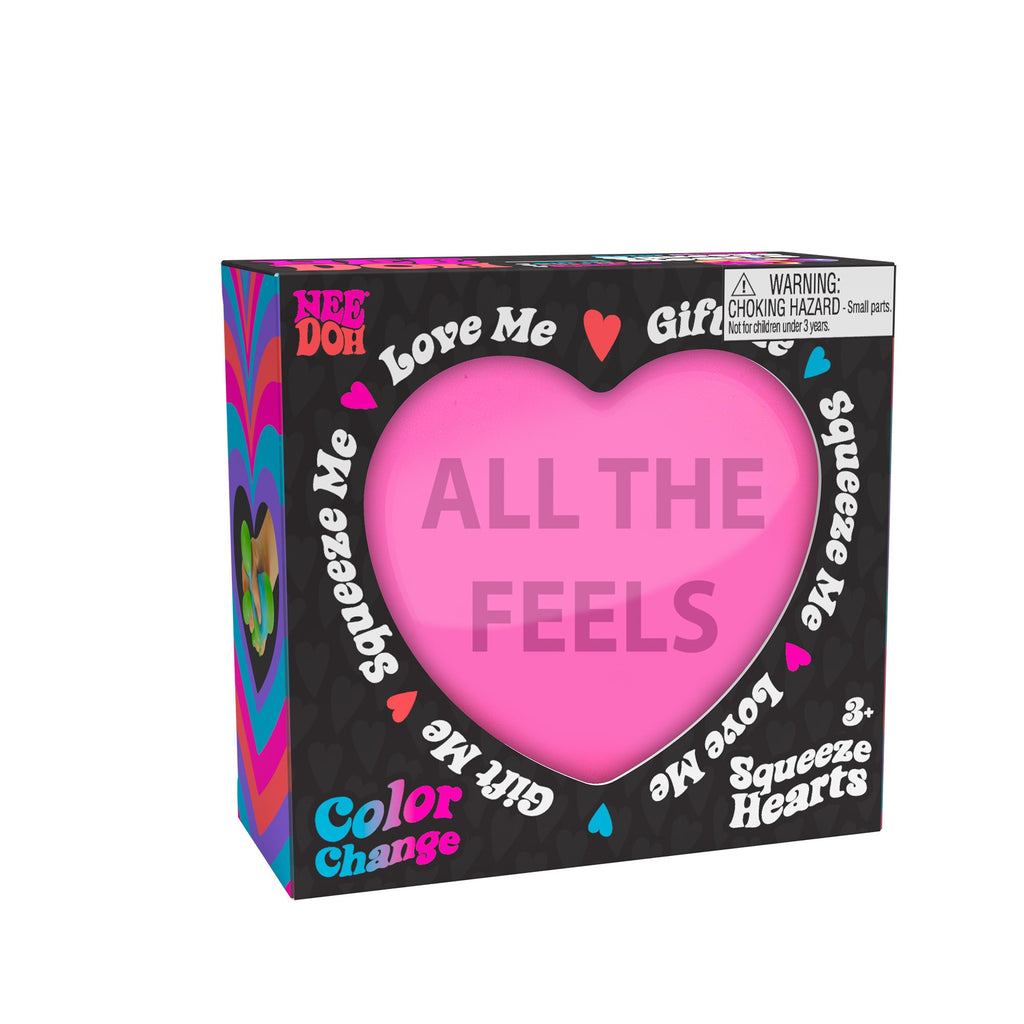 A boxed Nee Doh Color Change Squeeze Heart R2 toy. The packaging is predominantly black with colorful accents, featuring phrases like "ALL THE FEELS," "Squeeze Me," "Love Me," and "Gift Me." The box also includes a choking hazard warning for small parts.